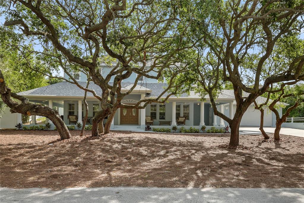 A two-story house with a wide front porch sits behind several large, mature oak trees — 6325 RIVER ROAD, NEW SMYRNA BEACH, FL