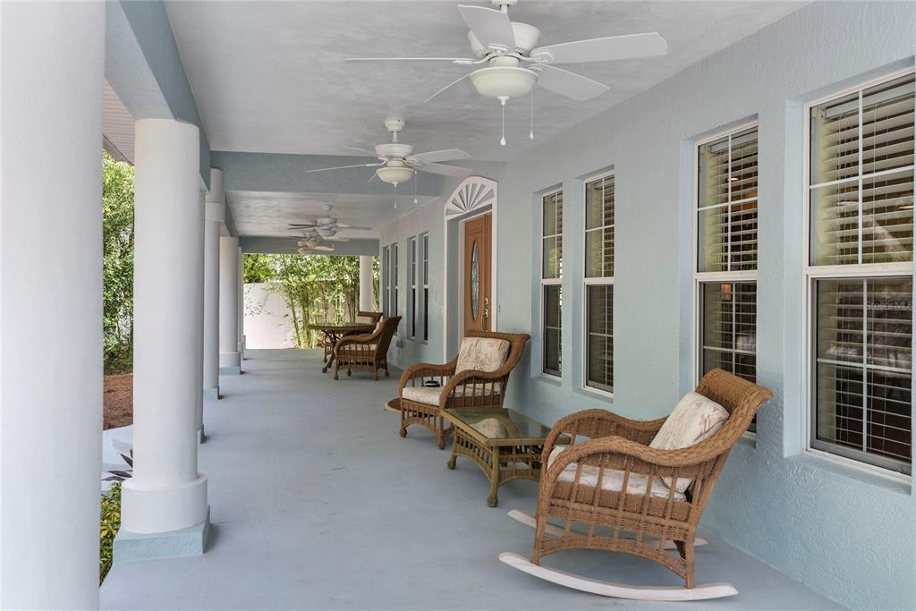 A covered porch features wicker furniture, ceiling fans, and white columns against a light-blue wall — 6325 RIVER ROAD, NEW SMYRNA BEACH, FL