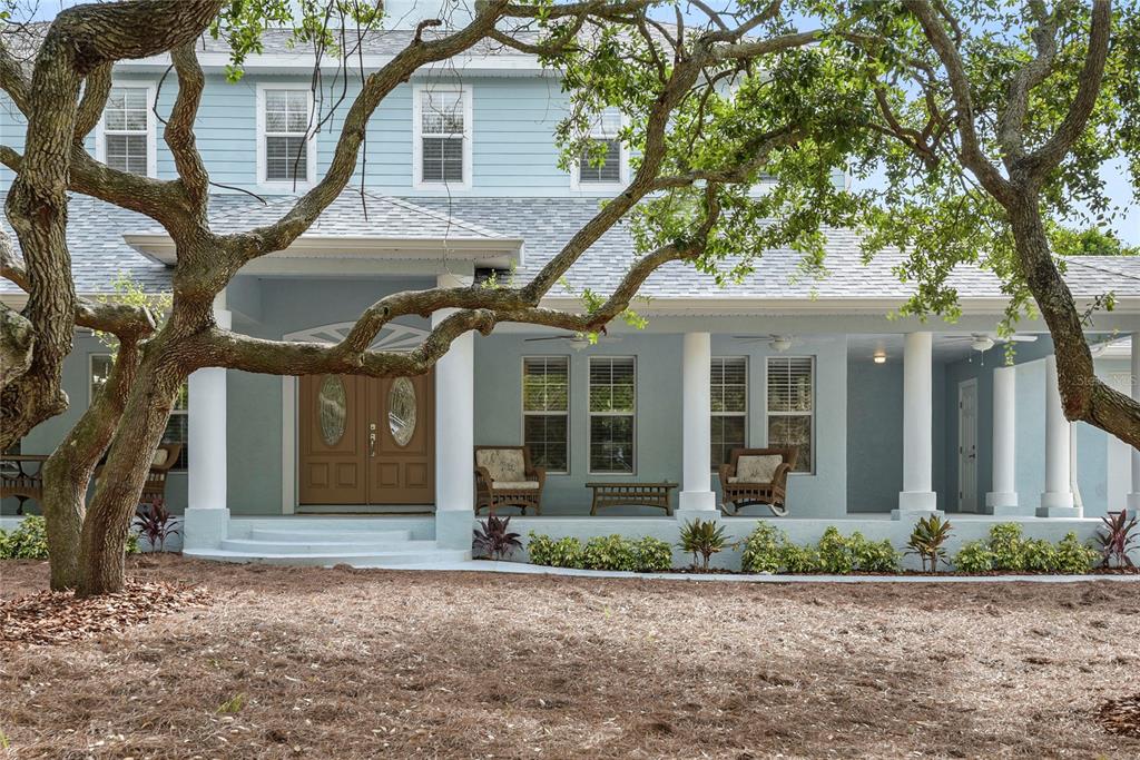 A light blue two-story house features a covered front porch with columns and wicker furniture — 6325 RIVER ROAD, NEW SMYRNA BEACH, FL