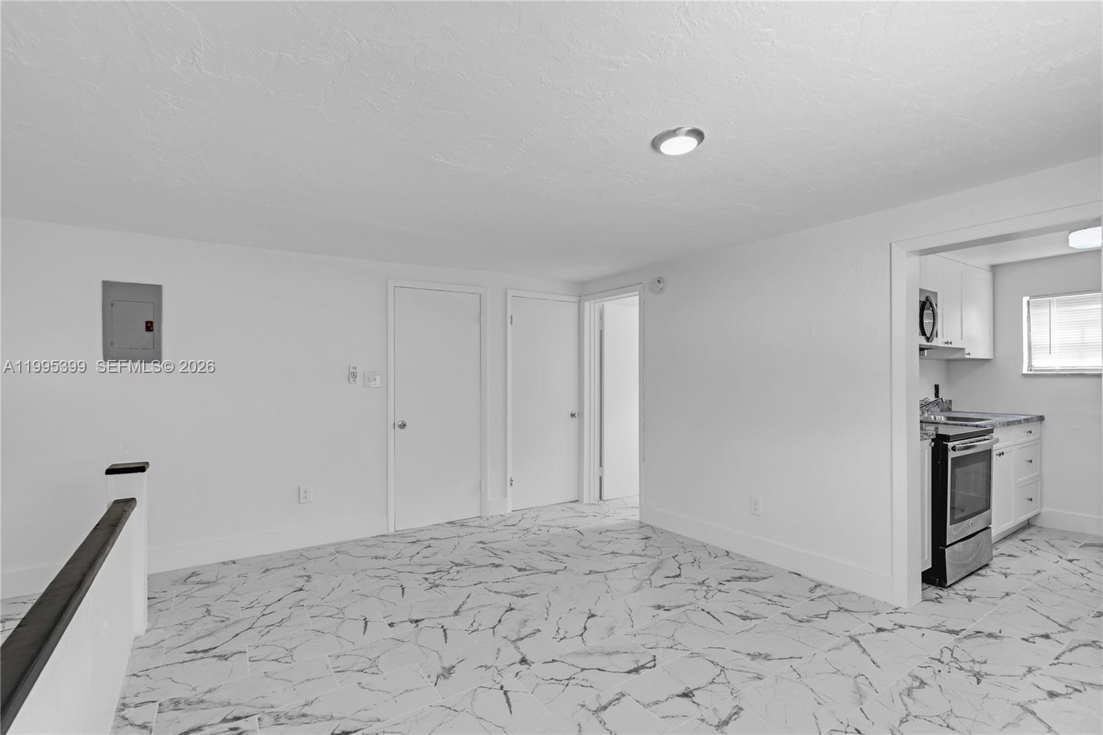 A room with white walls and marble-patterned tile flooring leads into a small kitchen — 56 NW 62nd St # 2, Miami FL 33150, MIAMI, FL