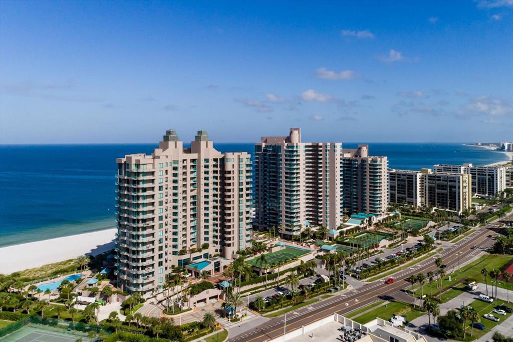 An aerial view shows two large beachfront condominium towers with tennis courts and a swimming pool — 1520 GULF BOULEVARD UNIT 1404, CLEARWATER BEACH, FL