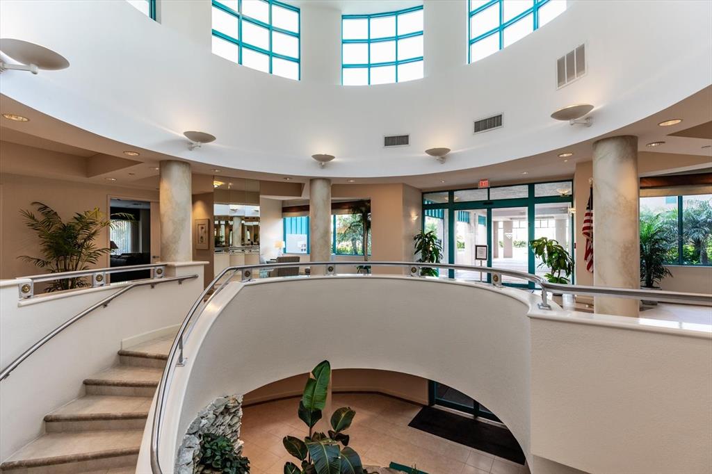 A curved staircase leads down into a bright lobby with a rotunda and large windows — 1520 GULF BOULEVARD UNIT 1404, CLEARWATER BEACH, FL