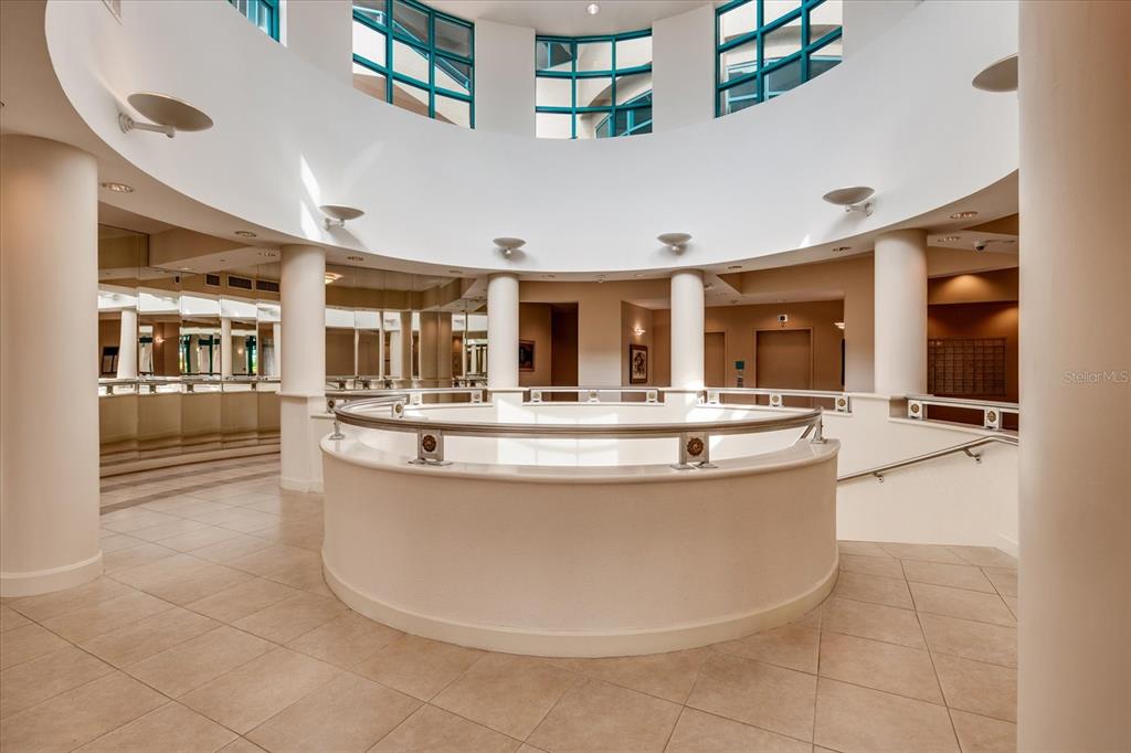 A circular atrium features a white curved railing, tiled floors, and large windows above — 1520 GULF BOULEVARD UNIT 1404, CLEARWATER BEACH, FL
