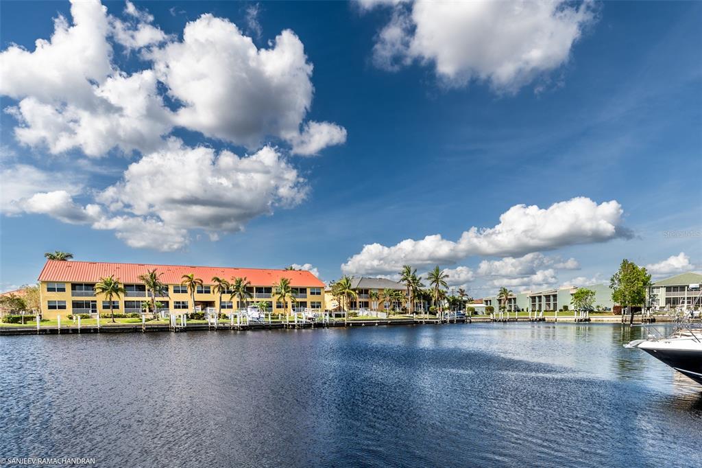 A waterfront apartment complex with a red roof sits along a canal under a cloudy sky — 3228 PURPLE MARTIN DRIVE DRIVE UNIT 125, PUNTA GORDA, FL