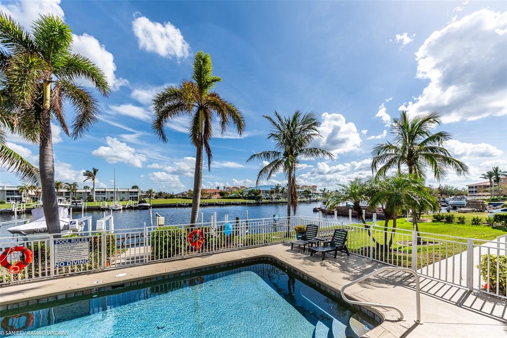 A swimming pool overlooks a canal with palm trees and residential buildings in the background — 3228 PURPLE MARTIN DRIVE DRIVE UNIT 125, PUNTA GORDA, FL