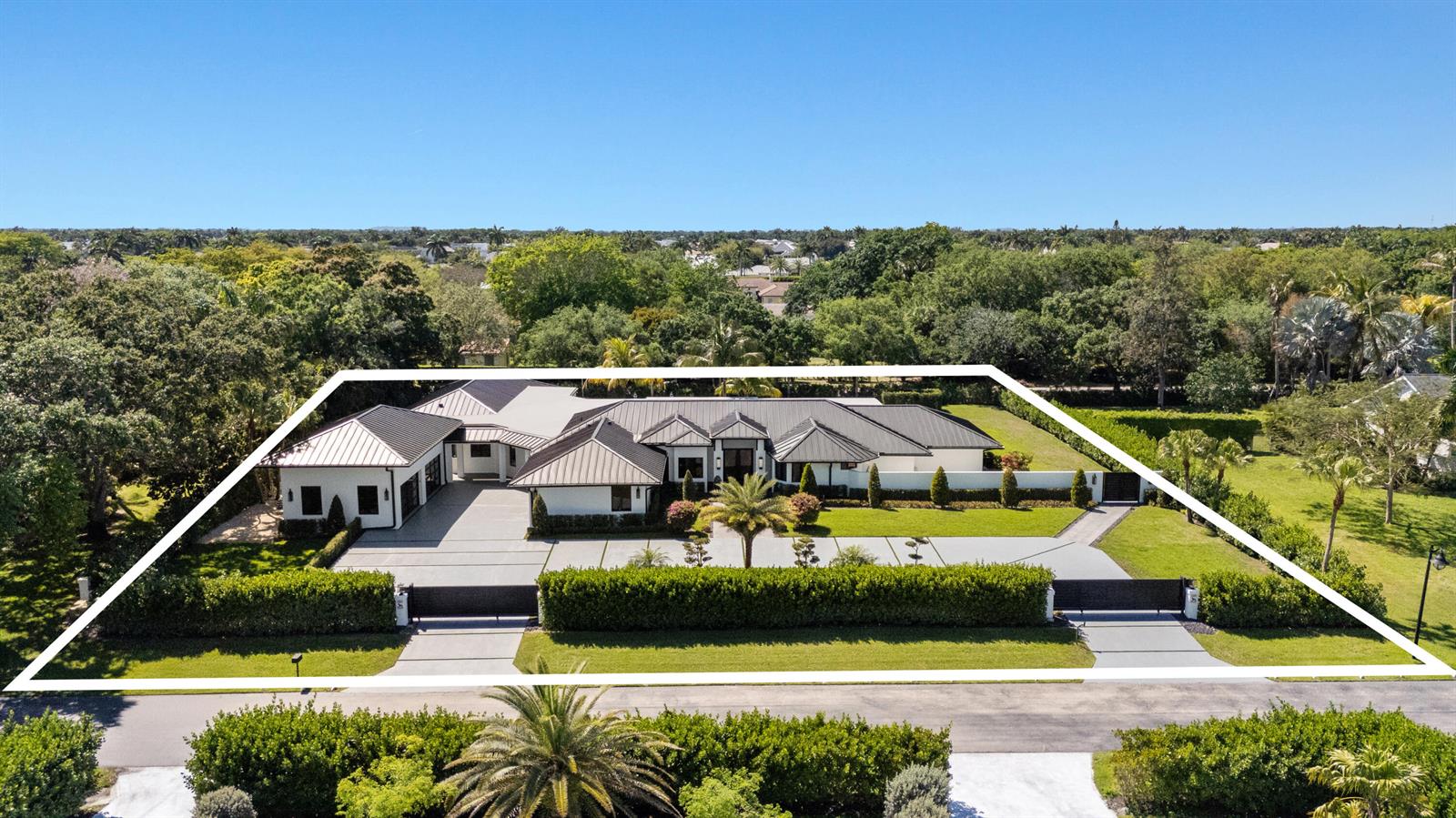 An aerial view shows a modern white house with a dark metal roof and gated driveway — 17872 W Fieldbrook Circle W, Boca Raton FL 33496, BOCA RATON, FL