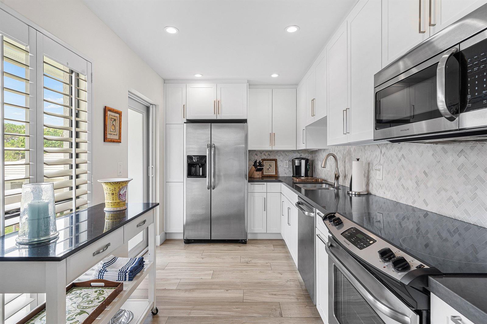 A modern kitchen features white cabinets, stainless steel appliances, dark countertops, and light wood flooring — 4285 B Quail Ridge Drive N, Boynton Beach FL 33436, BOYNTON BEACH, FL