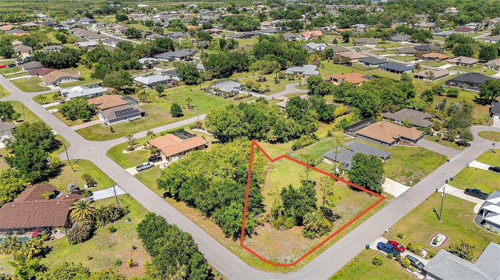 An aerial view shows a vacant, tree-covered residential lot outlined in red within a neighborhood — 27298 PORTO NACIONAL DRIVE, PUNTA GORDA, FL