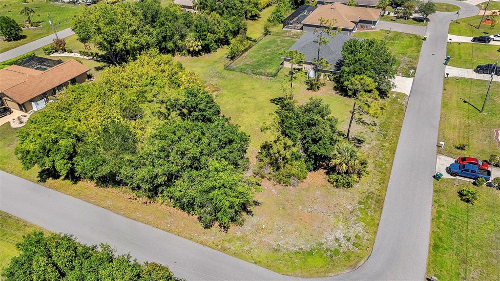 An aerial view shows a vacant, tree-covered residential lot situated between two houses on a street — 27298 PORTO NACIONAL DRIVE, PUNTA GORDA, FL