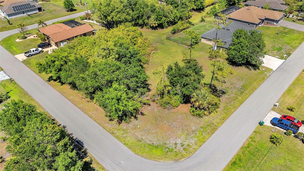 An aerial view shows a vacant, wooded residential lot situated at a street corner — 27298 PORTO NACIONAL DRIVE, PUNTA GORDA, FL