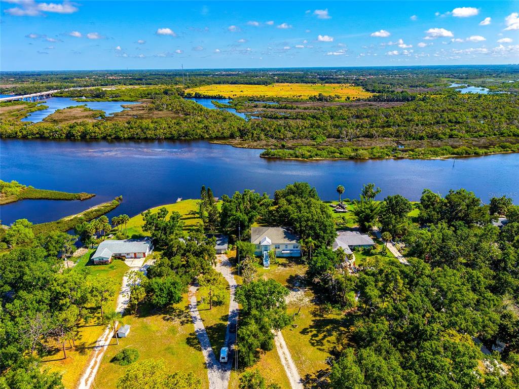 An aerial view shows houses surrounded by trees near a river and marshland — 11903 UPPER MANATEE RIVER ROAD, BRADENTON, FL