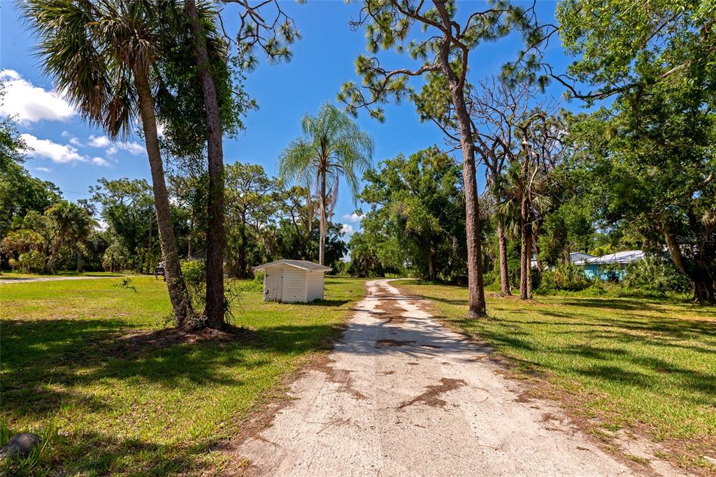 A dirt driveway leads past a small white shed toward trees on a sunny day — 11903 UPPER MANATEE RIVER ROAD, BRADENTON, FL