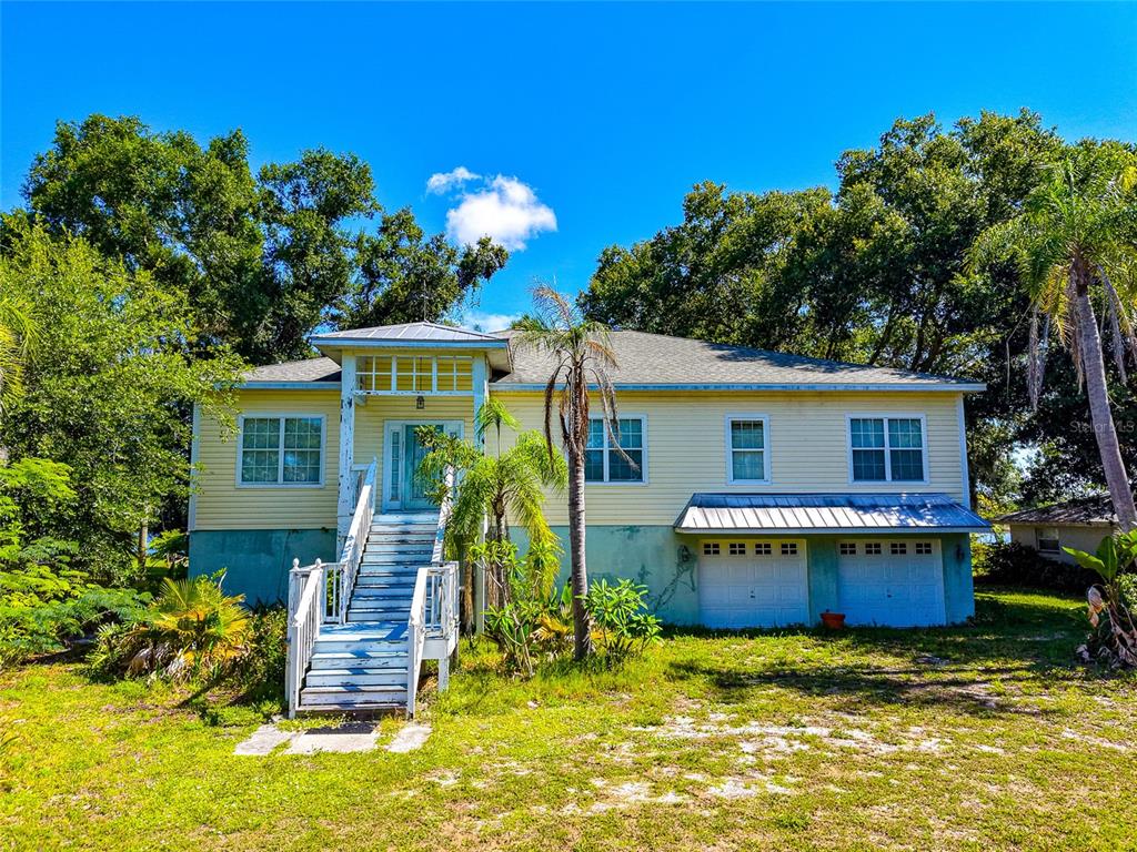 A two-story yellow house with a raised front entrance and a two-car garage below — 11903 UPPER MANATEE RIVER ROAD, BRADENTON, FL