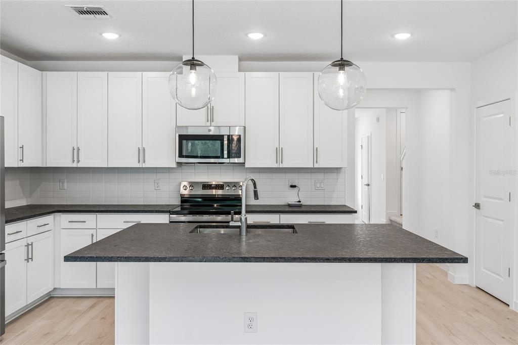 A modern kitchen features white cabinets, dark countertops, a central island, and stainless steel appliances — 3414 WITHERS WAY, DAVENPORT, FL