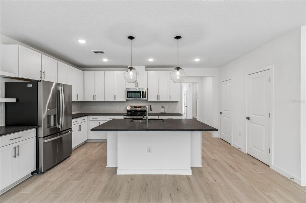 A modern kitchen features white cabinets, stainless steel appliances, and a dark-topped center island — 3414 WITHERS WAY, DAVENPORT, FL