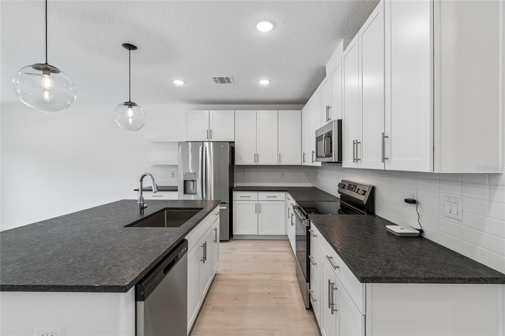 A modern kitchen features white cabinets, dark countertops, stainless steel appliances, and two pendant lights — 3414 WITHERS WAY, DAVENPORT, FL