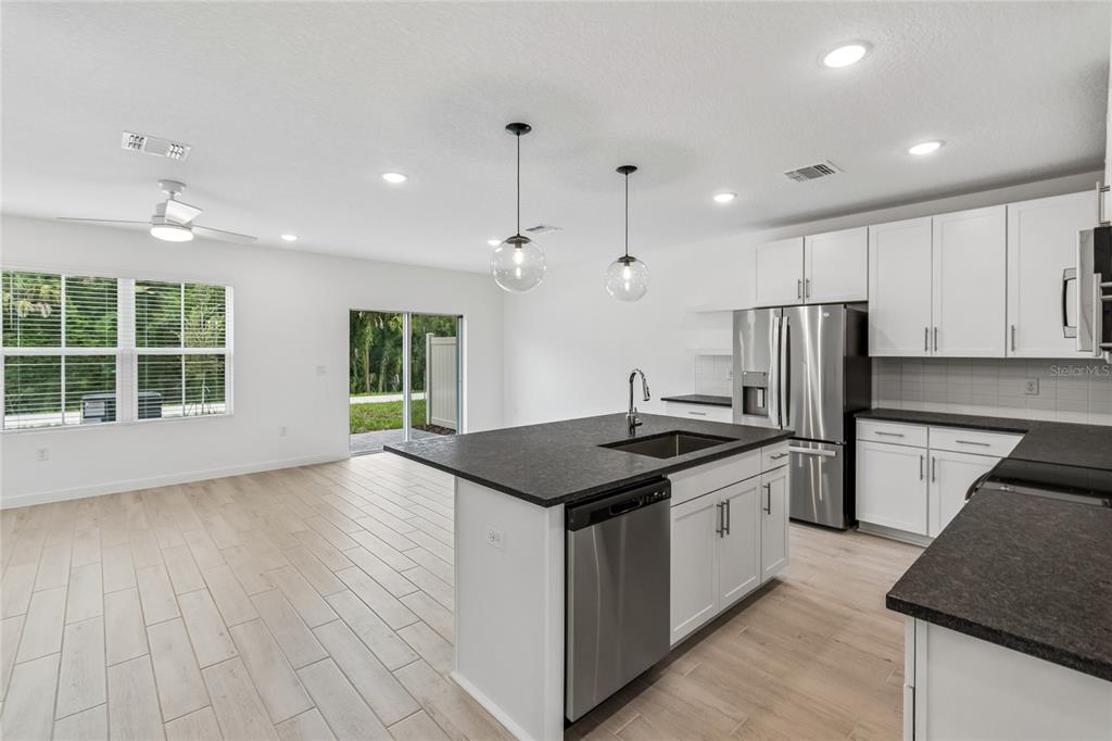A modern kitchen with white cabinets, dark countertops, and an island opens to a living area — 3414 WITHERS WAY, DAVENPORT, FL