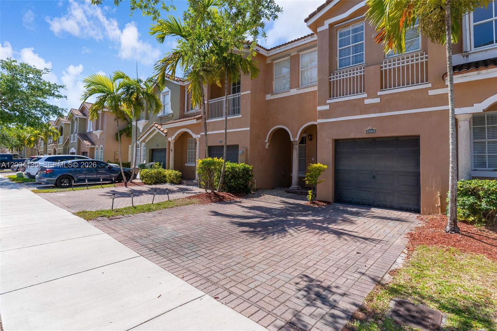 A row of two-story townhouses features paved driveways, attached garages, and palm trees — 2583 SE 13th Ct, Homestead FL 33035, HOMESTEAD, FL