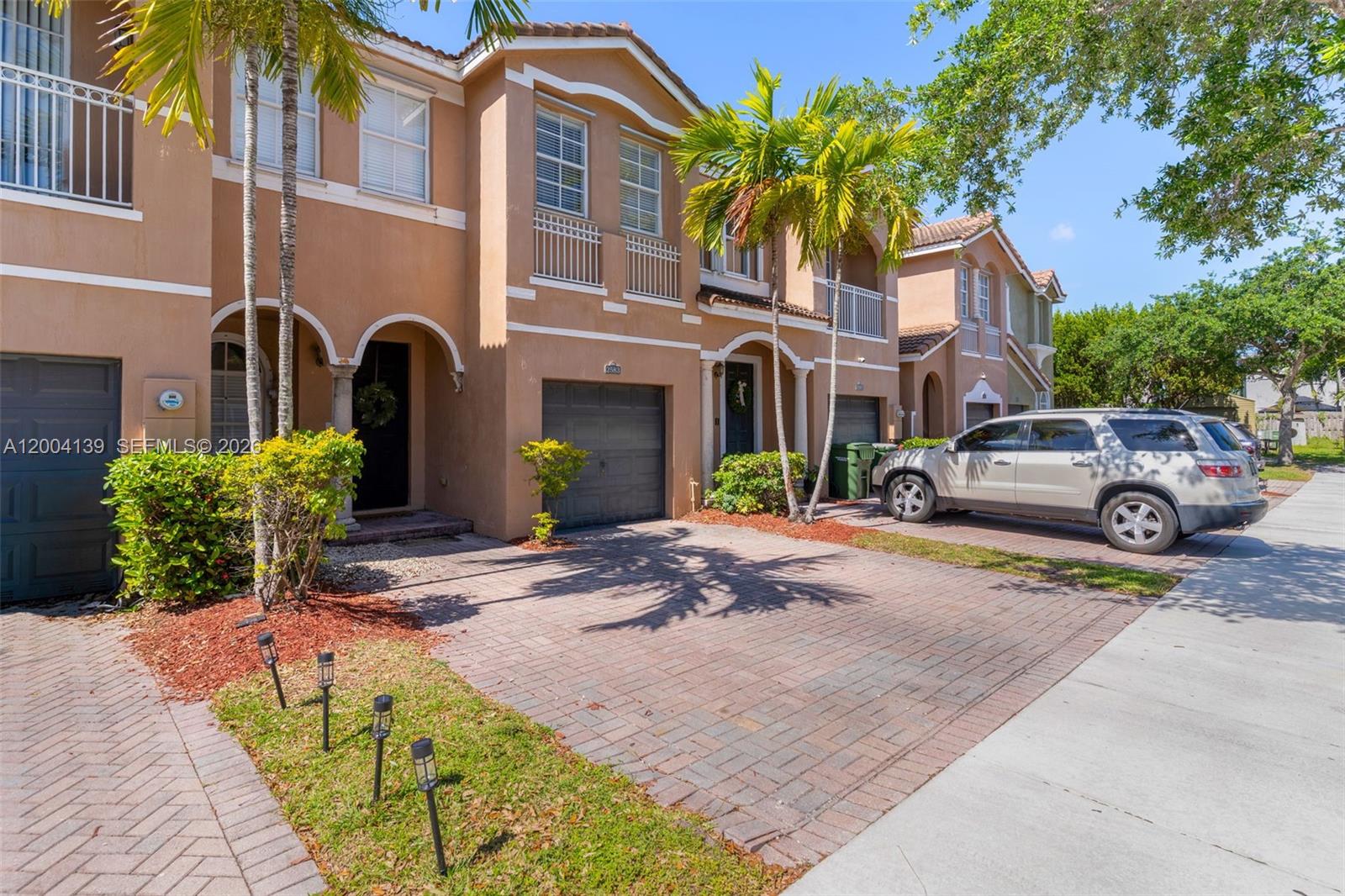 A row of two-story townhouses with tan stucco facades, arched entryways, and brick-paved driveways — 2583 SE 13th Ct, Homestead FL 33035, HOMESTEAD, FL