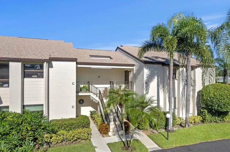 An exterior view of a two-story apartment building with a central staircase and palm trees — 702 Wingfoot Drive # D, Jupiter FL 33458, JUPITER, FL