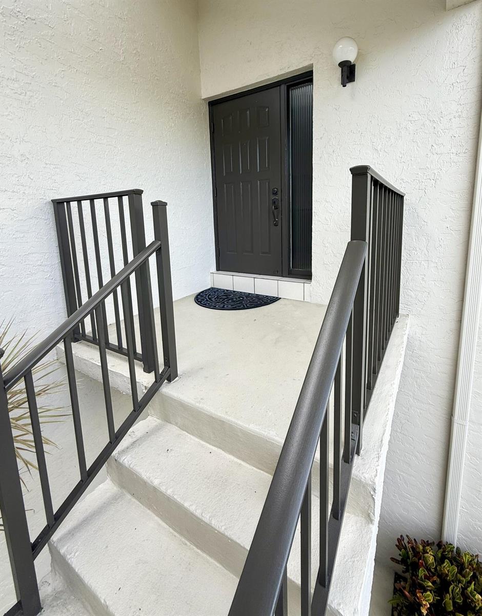 A concrete staircase with dark metal railings leads to a dark front door — 702 Wingfoot Drive # D, Jupiter FL 33458, JUPITER, FL
