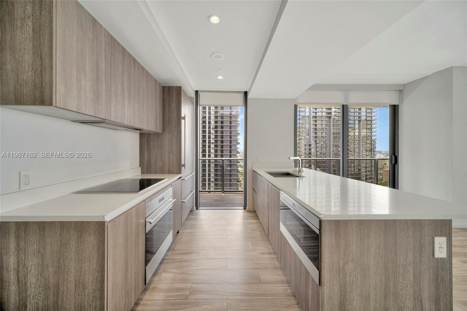 A modern kitchen features light wood cabinetry, white countertops, and a balcony with city views — 801 S Miami Ave # 2909, Miami FL 33130, MIAMI, FL