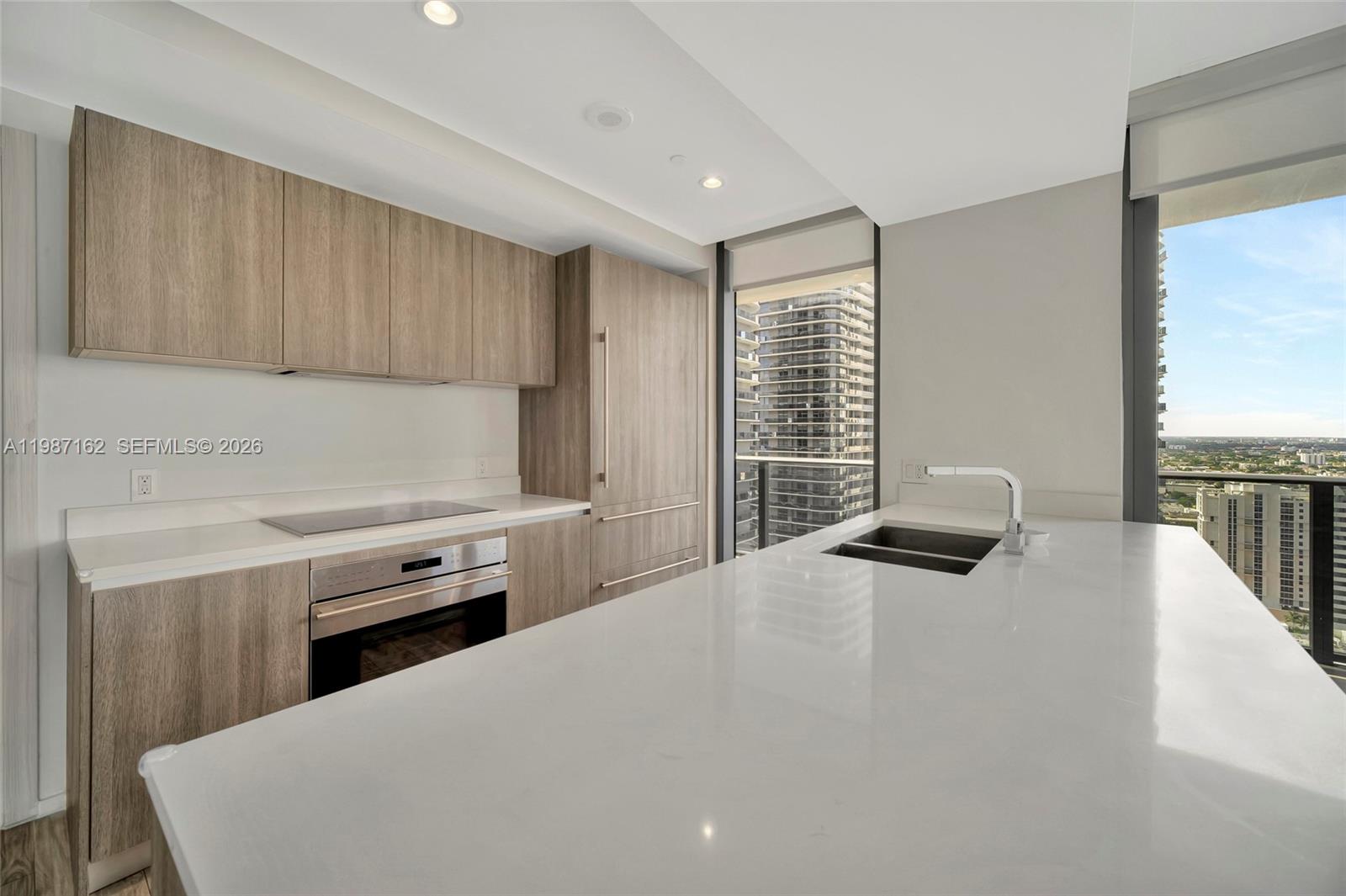 A modern kitchen features light wood cabinetry, white countertops, and a view of city buildings — 801 S Miami Ave # 2909, Miami FL 33130, MIAMI, FL