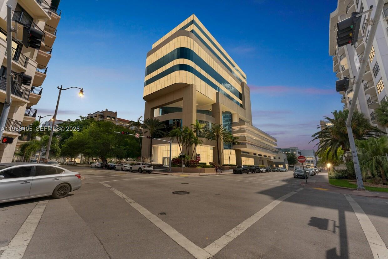 A modern office building stands at a street intersection with palm trees and parked cars — 75 Valencia Ave # 302, Coral Gables FL 33134, CORAL GABLES, FL