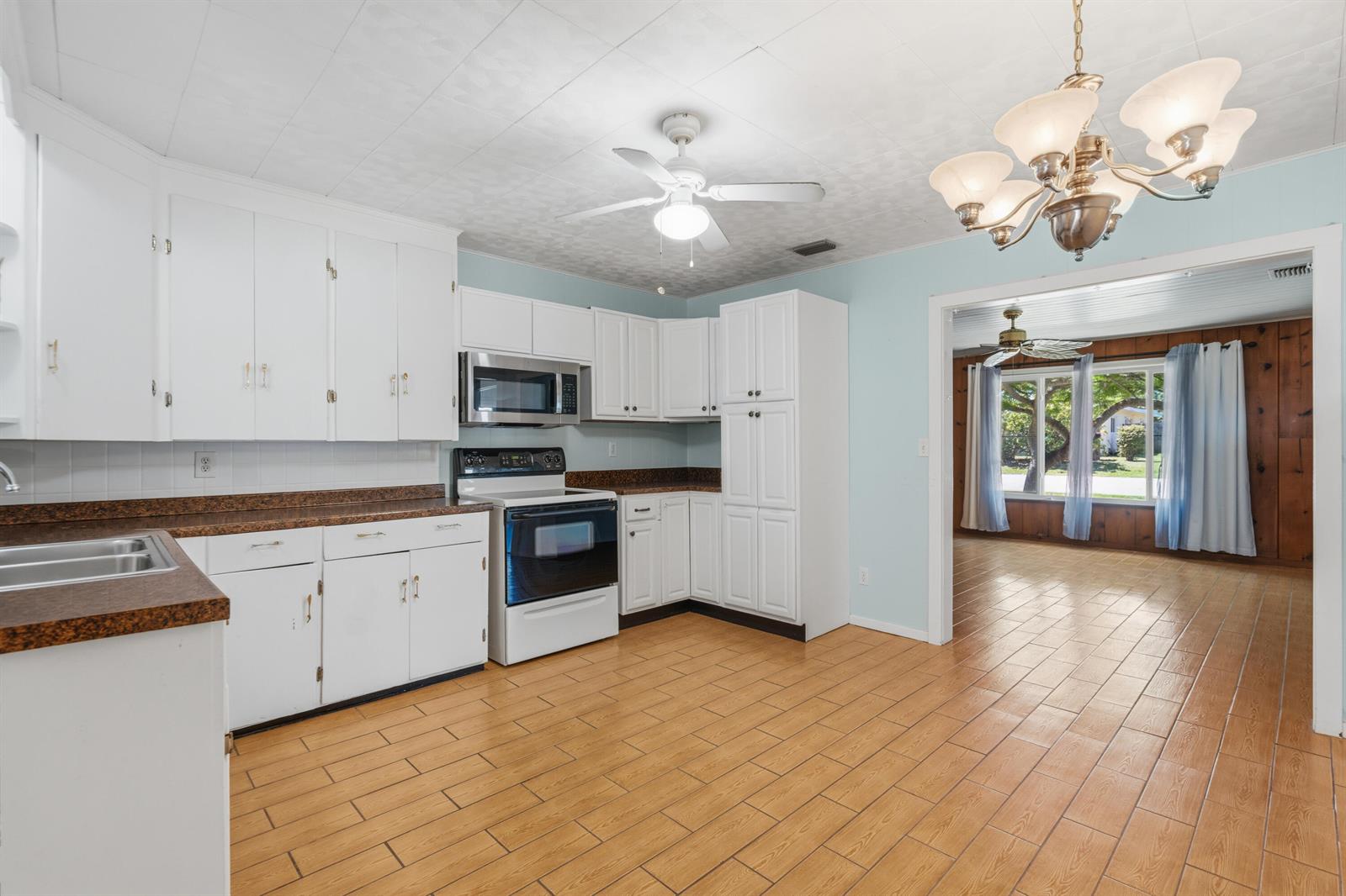 A kitchen with white cabinets, brown countertops, and tile flooring opens into a living area — 1404 Binney Drive, Fort Pierce FL 34949, FORT PIERCE, FL