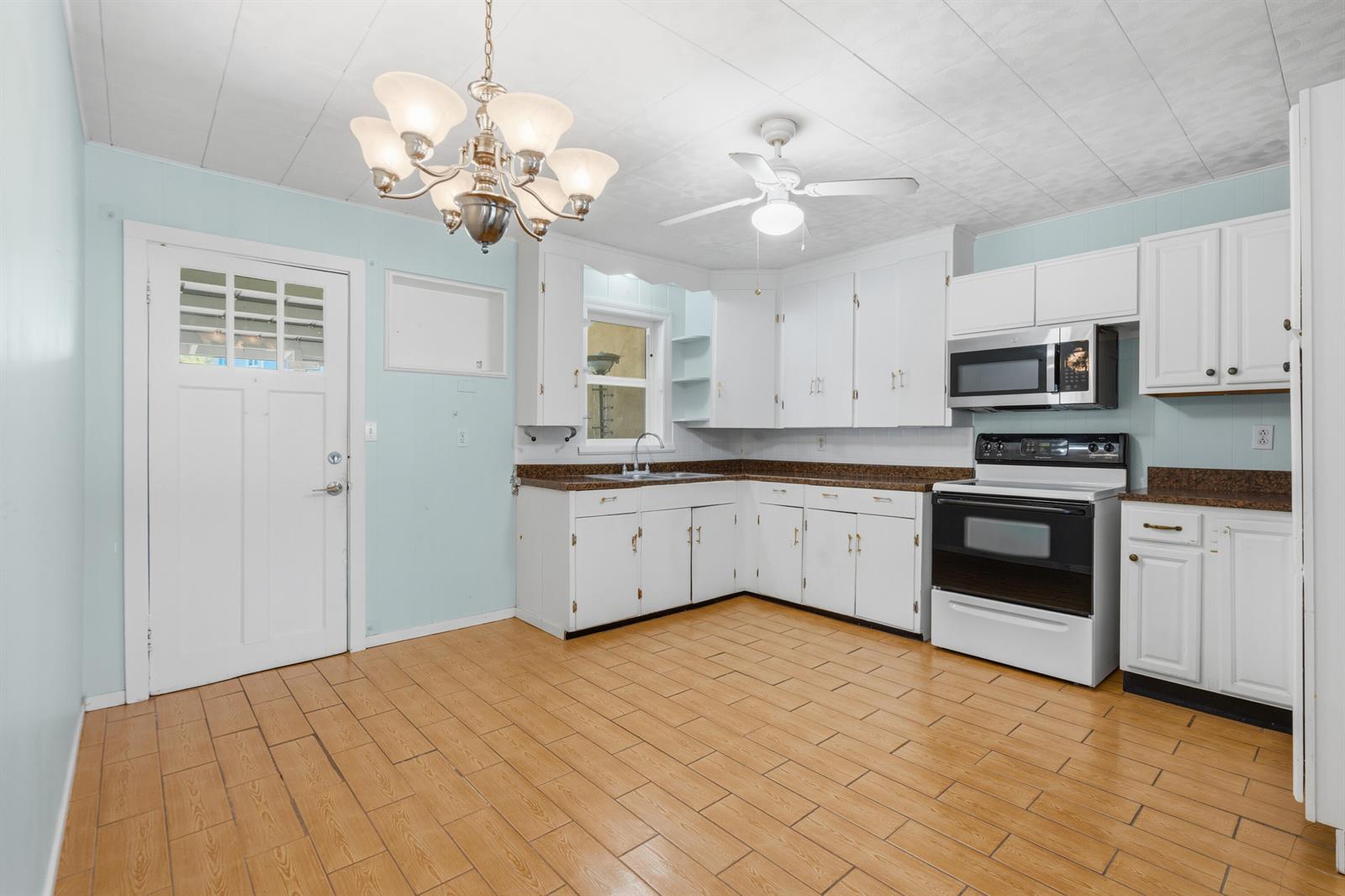 A kitchen features white cabinets, a dark countertop, light blue walls, and wood-look tile flooring — 1404 Binney Drive, Fort Pierce FL 34949, FORT PIERCE, FL