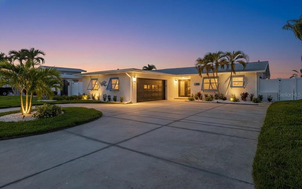 A single-story house with a concrete driveway, a two-car garage, and palm trees at dusk — 510 115TH AVENUE, TREASURE ISLAND, FL
