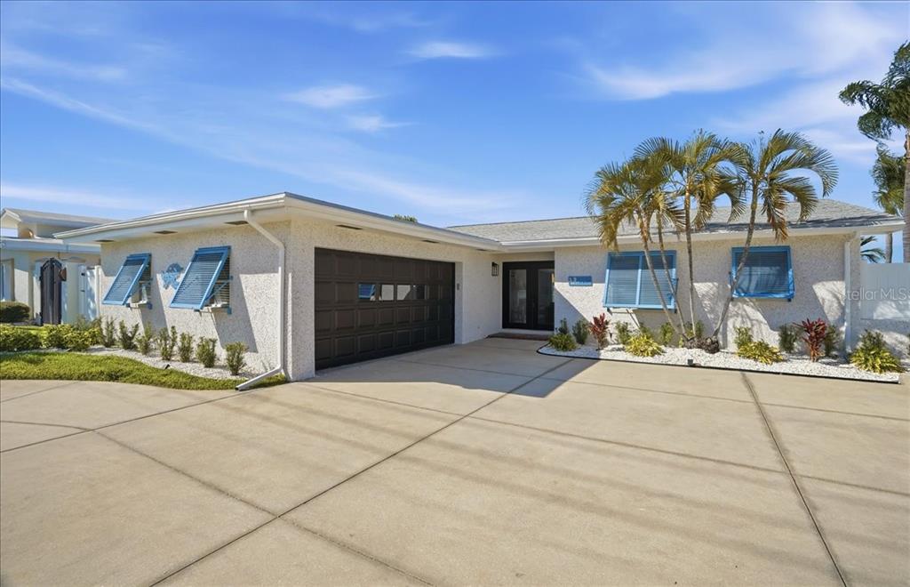 A single-story house with a white stucco exterior, a dark garage door, and palm trees — 510 115TH AVENUE, TREASURE ISLAND, FL