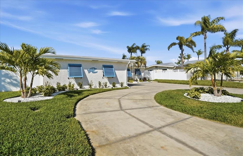 A single-story house with a curved concrete driveway, blue shutters, and palm trees in front — 510 115TH AVENUE, TREASURE ISLAND, FL