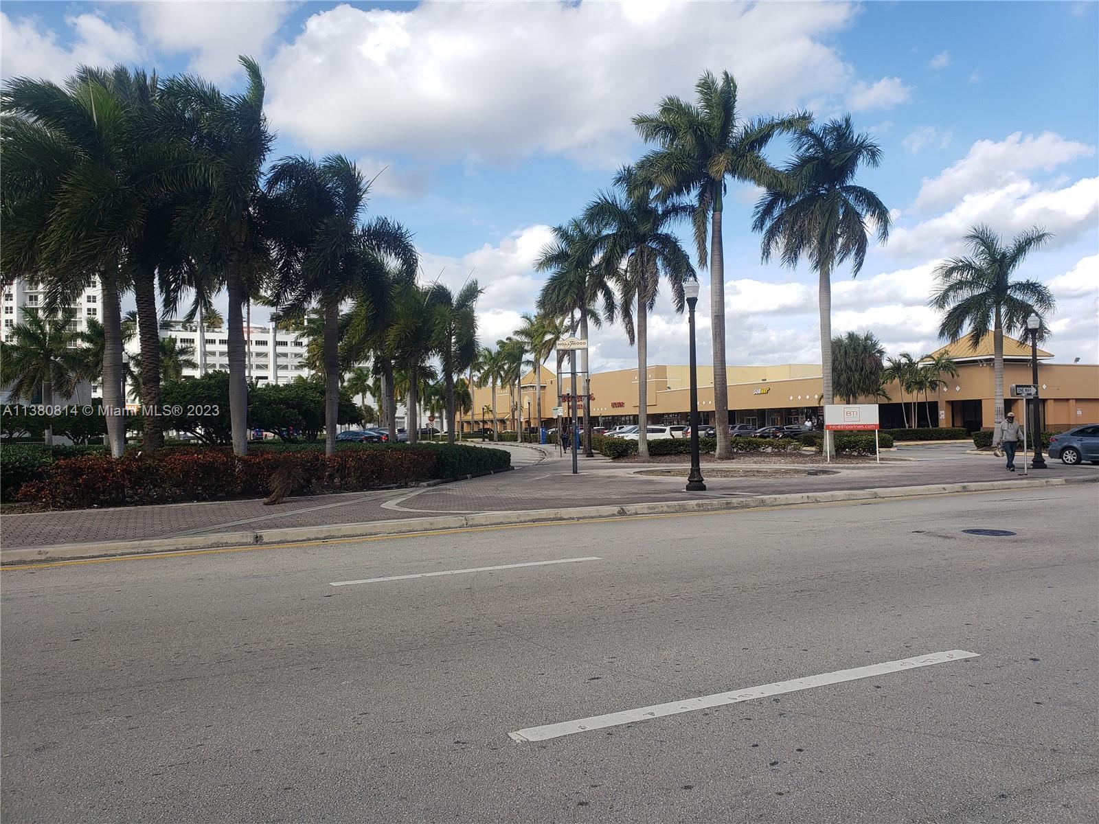 A parking lot and shopping center are lined with palm trees under a cloudy sky — 1720 Harrison St # 12D, Hollywood FL 33020, HOLLYWOOD, FL