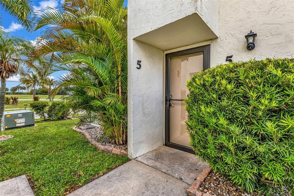 A view of a building entrance with a number five, a glass door, and landscaping — 1001 W MARION AVENUE UNIT 5, PUNTA GORDA, FL