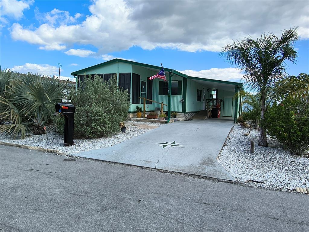 A light green manufactured home features a screened porch, a carport, and a paved driveway — 7306 GRAND PINE DRIVE, HUDSON, FL