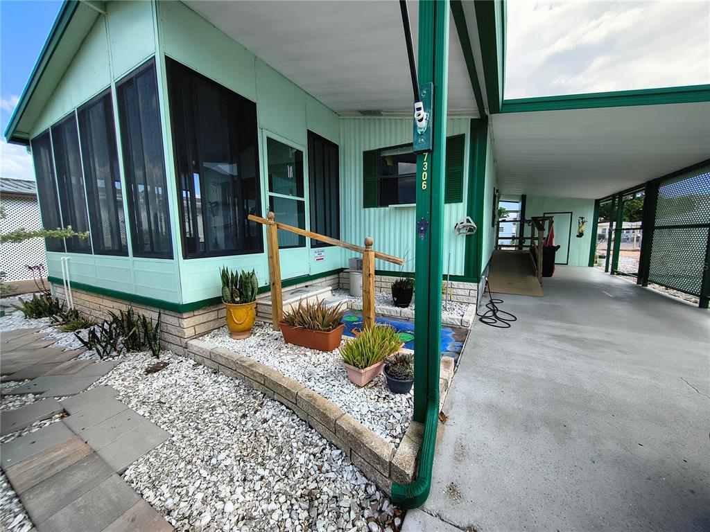 A light green mobile home exterior features a screened porch, carport, and landscaped rock garden — 7306 GRAND PINE DRIVE, HUDSON, FL