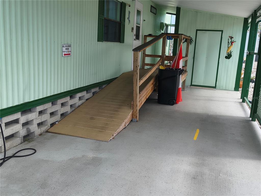 A wooden wheelchair ramp leads to the side entrance of a light green mobile home — 7306 GRAND PINE DRIVE, HUDSON, FL