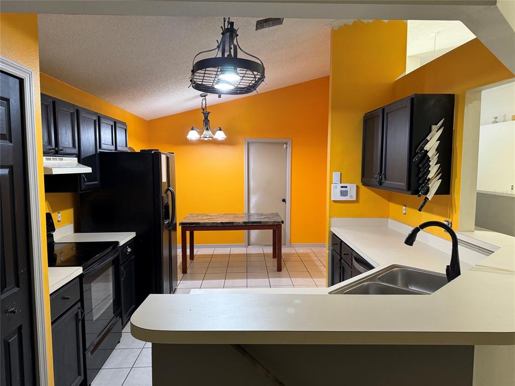 A kitchen features black cabinets, a black refrigerator, a dining table, and bright orange walls — 815 DELFINO PLACE, LAKE MARY, FL