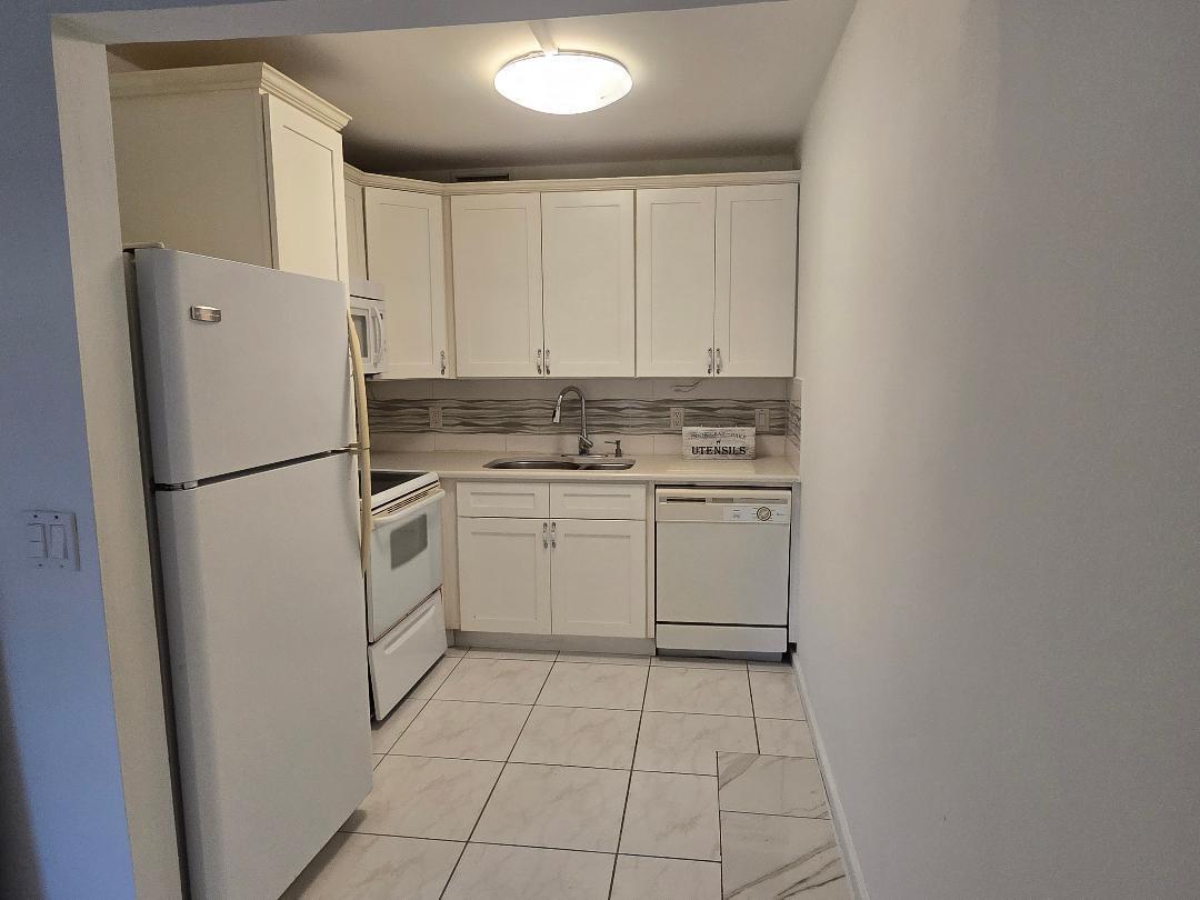 A kitchen features white cabinets, white appliances, a tiled floor, and a tiled backsplash — 227 Kent N, West Palm Beach FL 33417, WEST PALM BEACH, FL