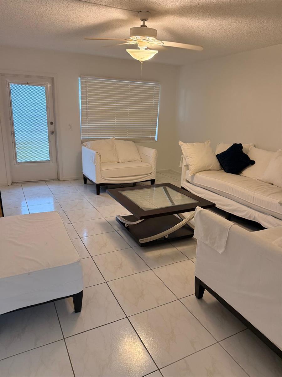 A living room features white furniture, a glass-topped coffee table, and light-colored tile flooring — 227 Kent N, West Palm Beach FL 33417, WEST PALM BEACH, FL