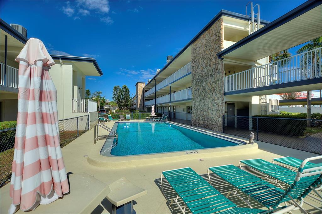 A rectangular swimming pool sits between two multi-story apartment buildings with outdoor lounge chairs — 6100 12TH STREET S UNIT 221, ST PETERSBURG, FL