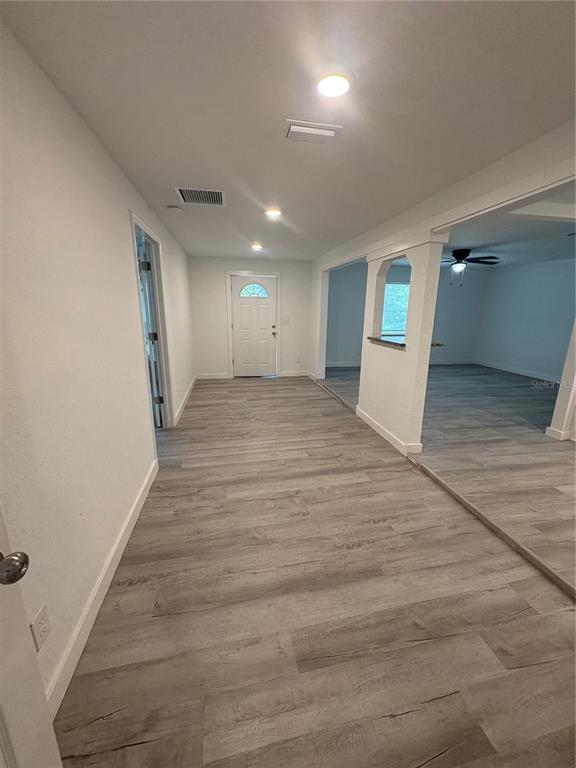 A hallway with light wood-look flooring leads to an exterior door and an adjacent room — 312 SE 49TH DRIVE, GAINESVILLE, FL