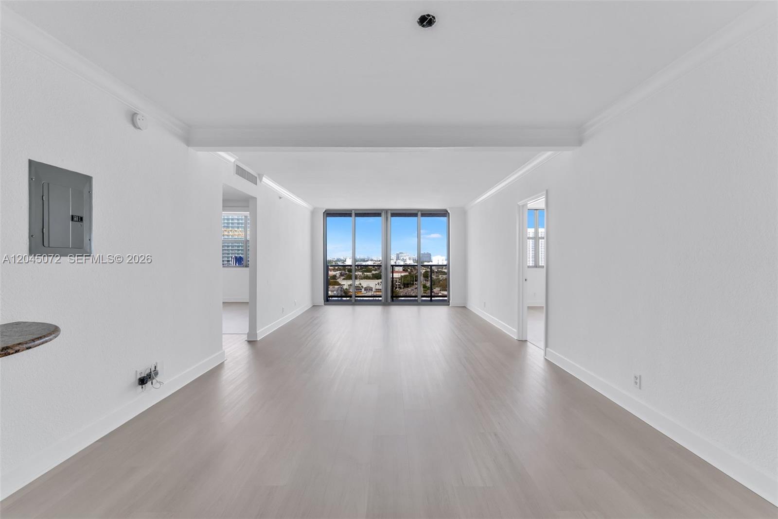 An empty, white-walled living area features light wood flooring and large floor-to-ceiling windows — 401 69th St # 1201, Miami Beach FL 33141, MIAMI BEACH, FL