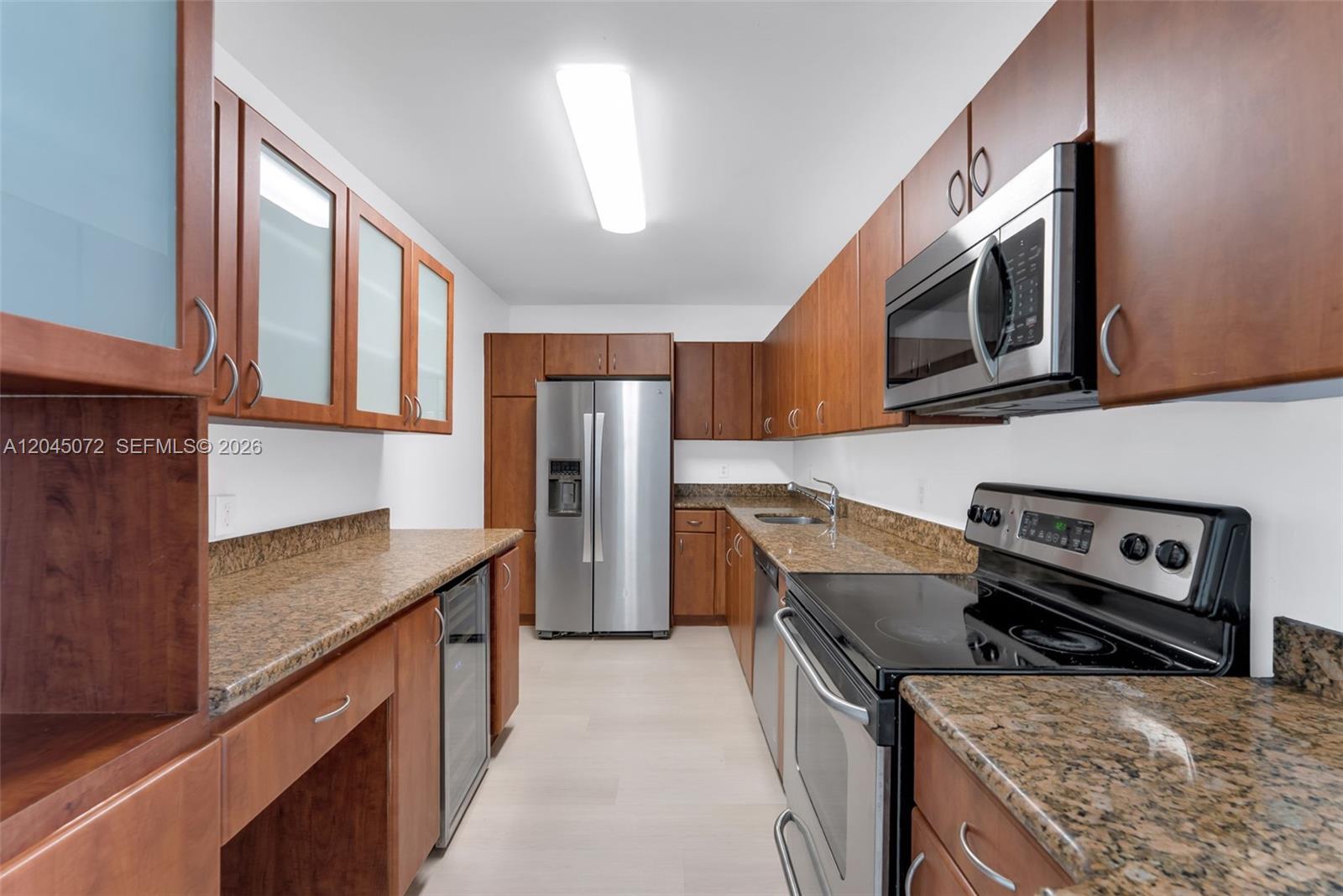 A galley kitchen features wood cabinets, granite countertops, and stainless steel appliances — 401 69th St # 1201, Miami Beach FL 33141, MIAMI BEACH, FL