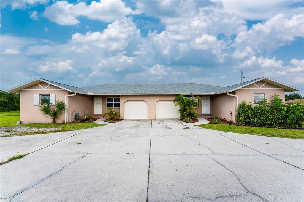 A single-story duplex with two garage doors and a large concrete driveway under a sky — 51 BOUNDARY BOULEVARD UNIT B, ROTONDA WEST, FL