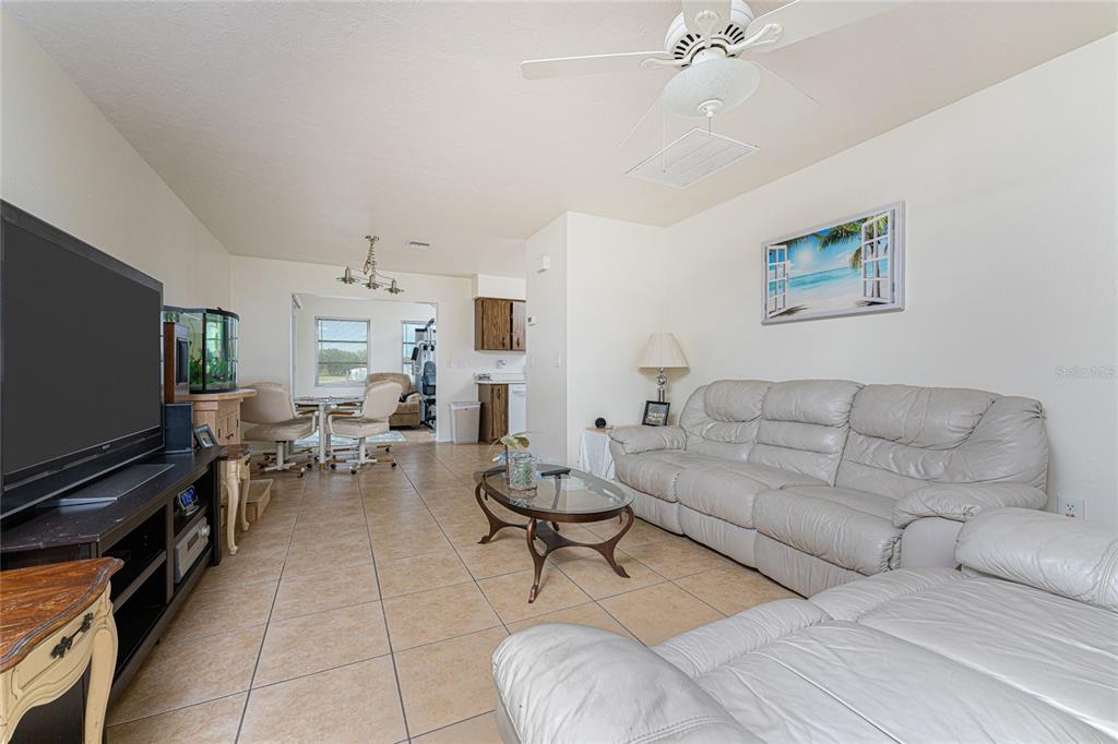 A living room features light-colored tile flooring, a white leather sofa, and a ceiling fan — 51 BOUNDARY BOULEVARD UNIT B, ROTONDA WEST, FL