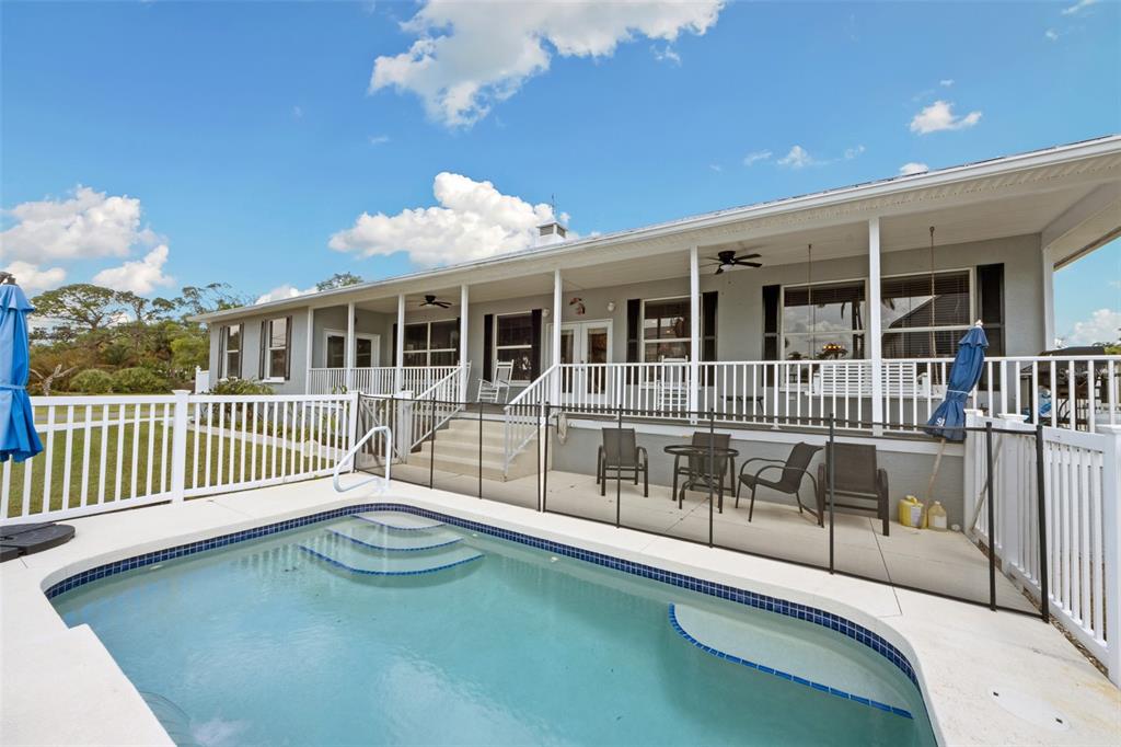 A swimming pool sits in front of a house with a covered porch and white railing — 310 13TH AVENUE W, PALMETTO, FL