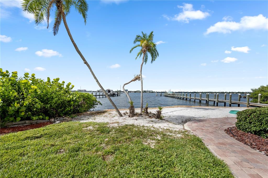 A sandy waterfront yard features two palm trees, a wooden dock, and a brick walkway — 310 13TH AVENUE W, PALMETTO, FL