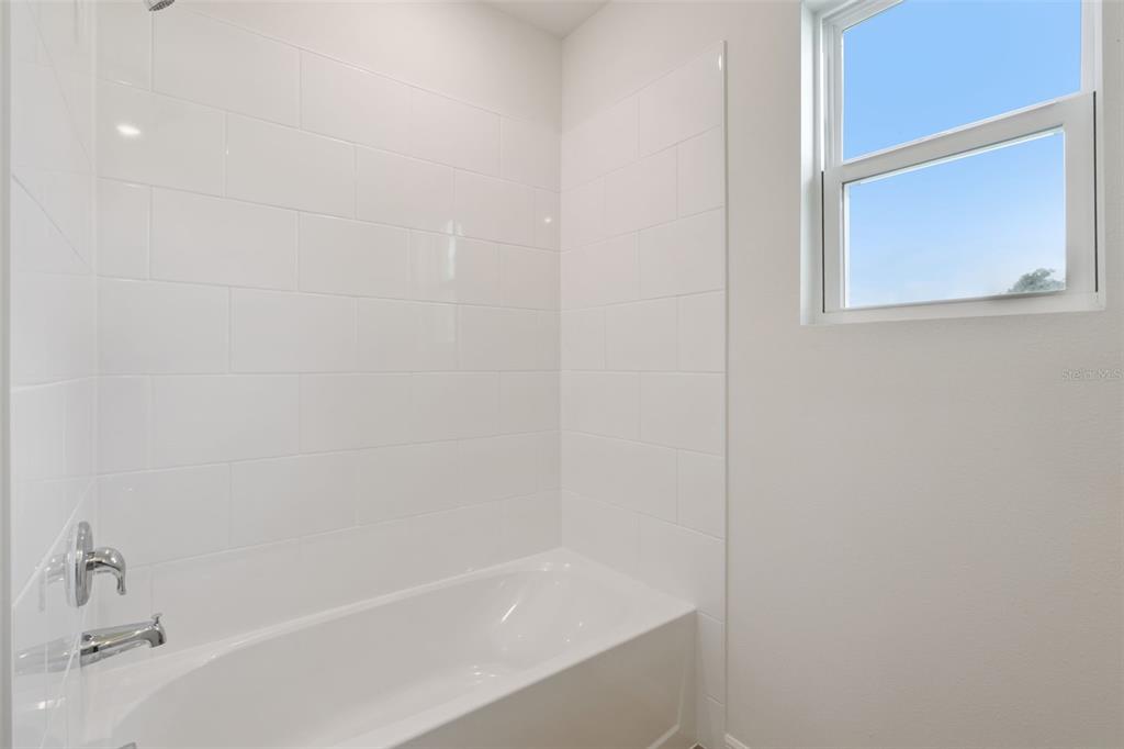 A white bathtub with subway tile surround and a window in a bathroom — 2514 DORSET COURT, ORMOND BEACH, FL